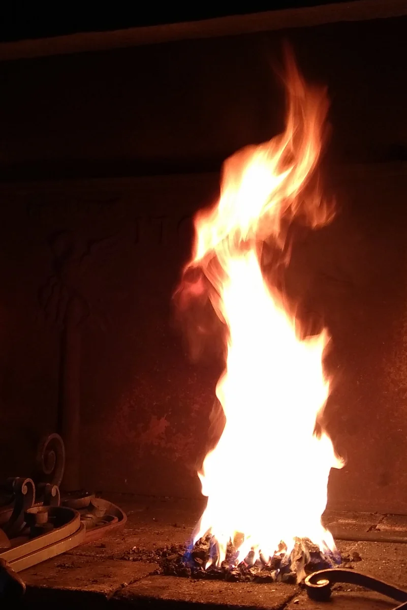 Flammes vives du feu de forge au-dessus des braises, outils au premier plan