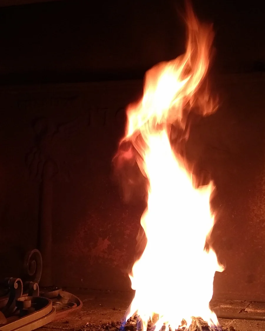 Flammes vives du feu de forge au-dessus des braises, outils au premier plan