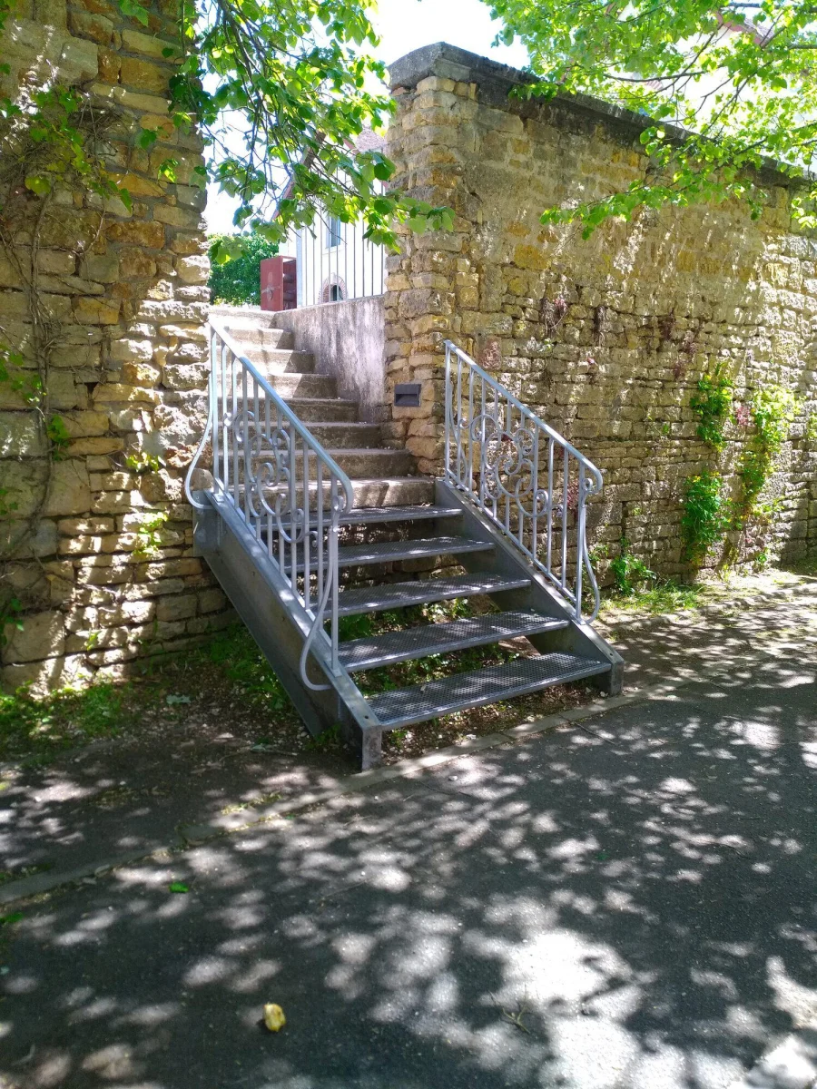Rampe d’escalier extérieur en acier, posée sur un escalier de pierre entre deux murs anciens